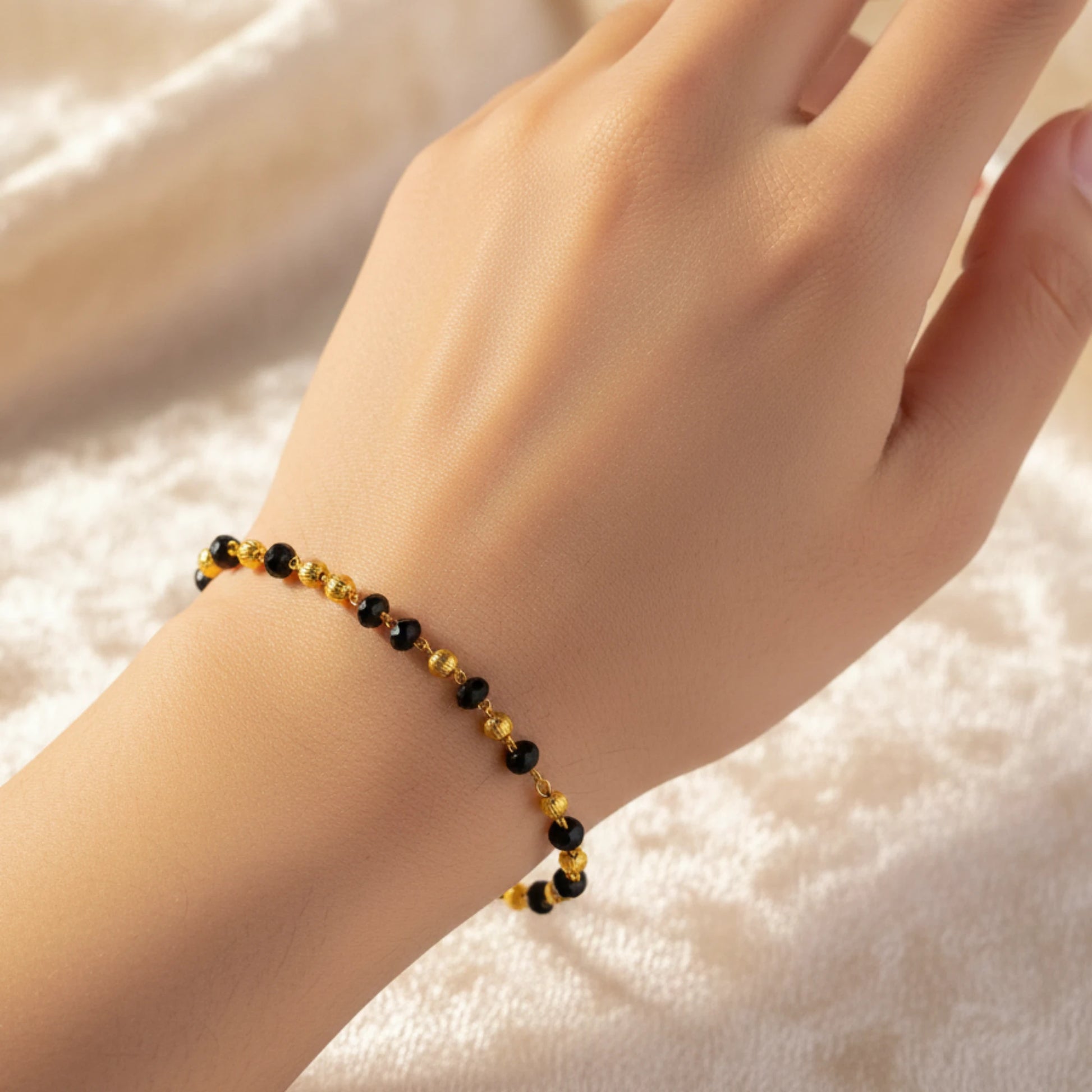 Hand wearing a black beaded gold plated bracelet on a soft white background