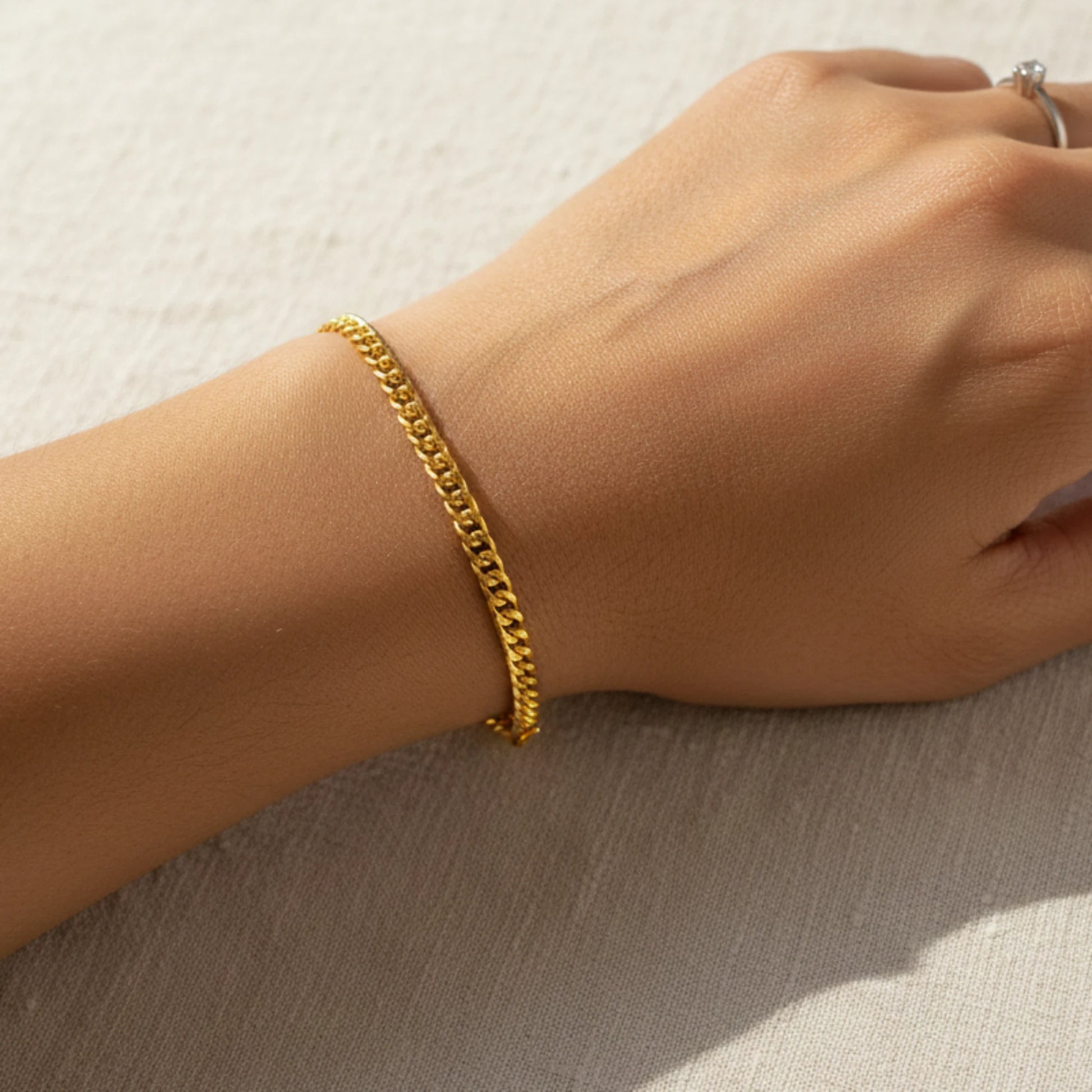 Gold plated curb link chain bracelet on a wrist against a neutral background