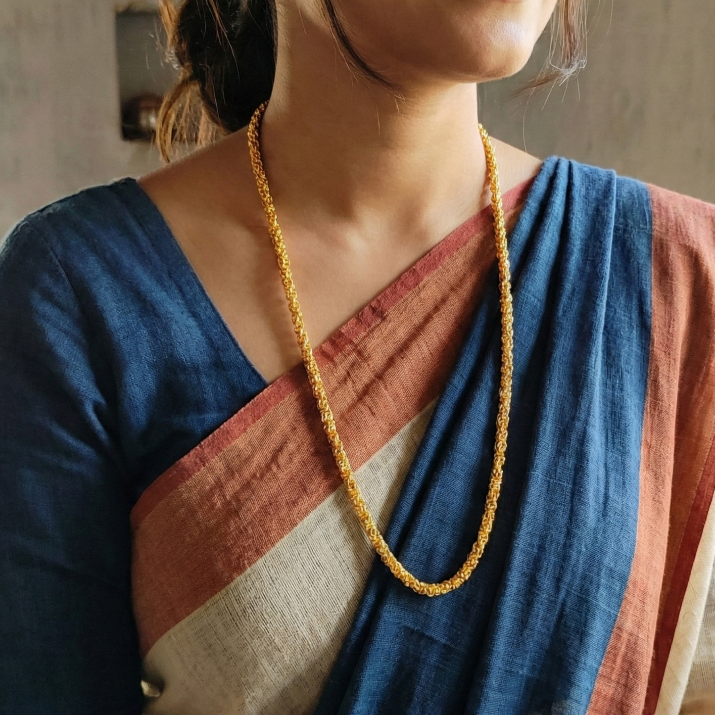 Person wearing a blue and brown saree with a gold plated neck chain