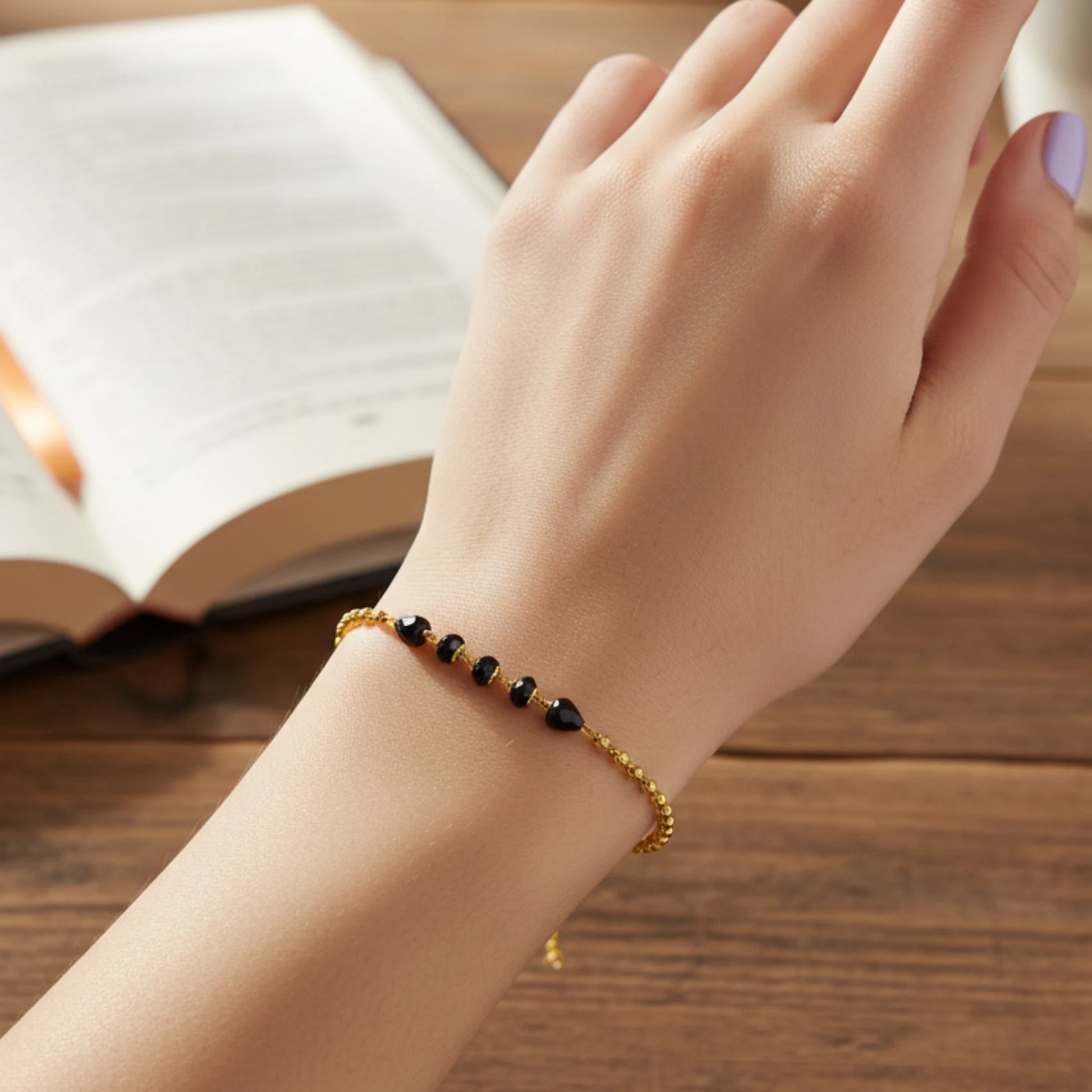 Hand wearing a gold plated bracelet with black beads on a wooden surface with an open book.