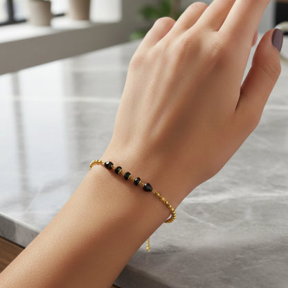 Hand wearing a gold plated bracelet with black beads on a neutral background
