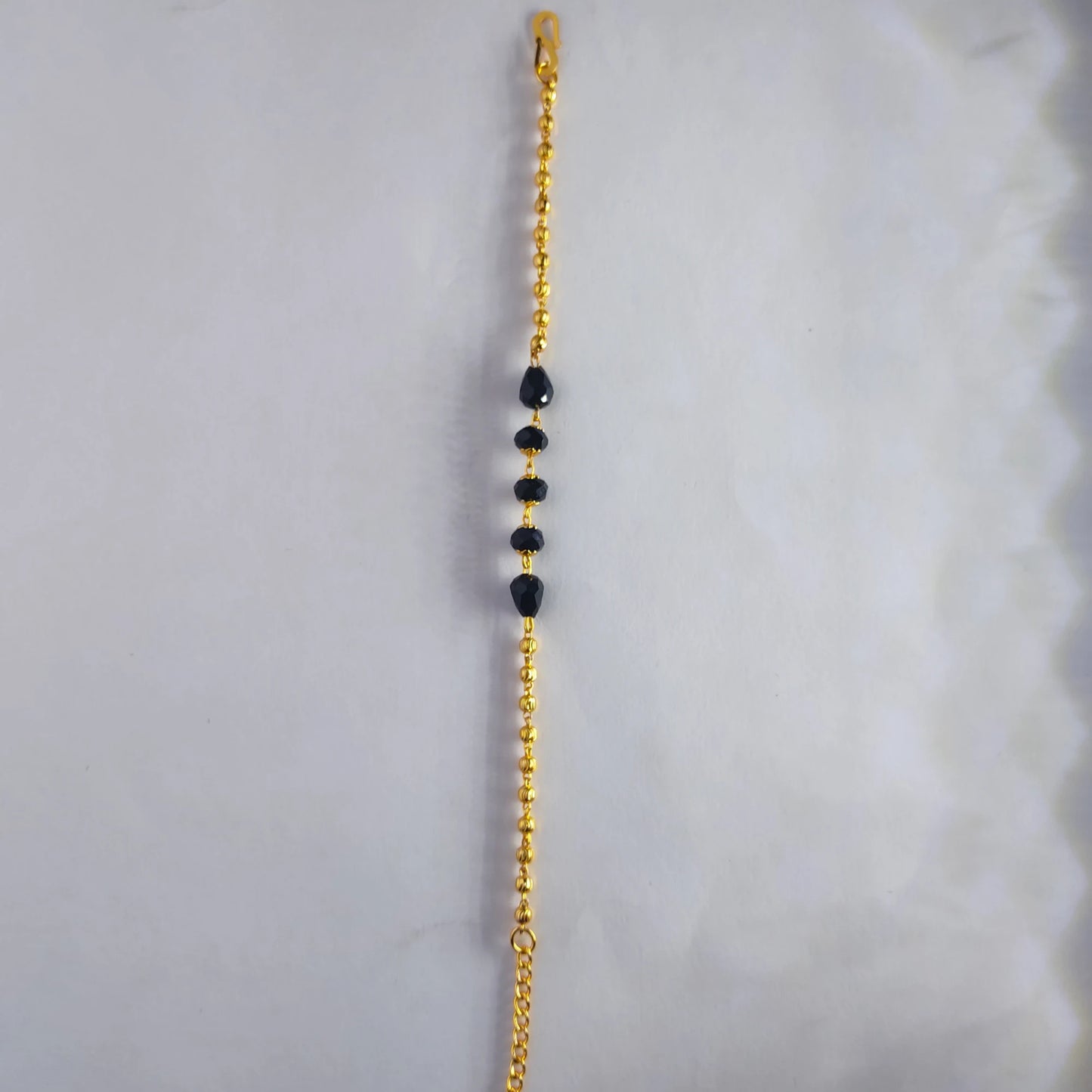 Gold plated bracelet chain with black beads on a white background
