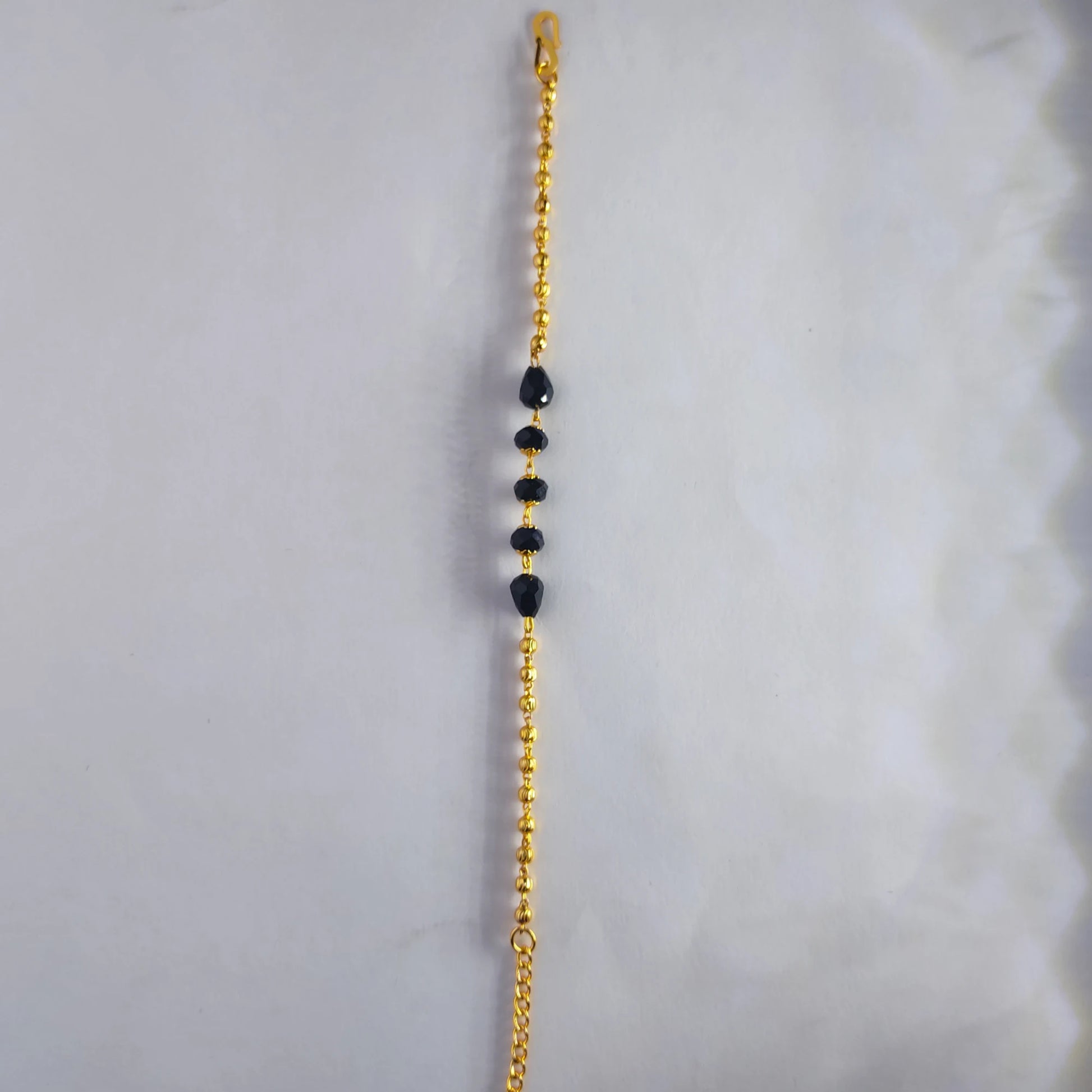 Gold plated bracelet chain with black beads on a white background