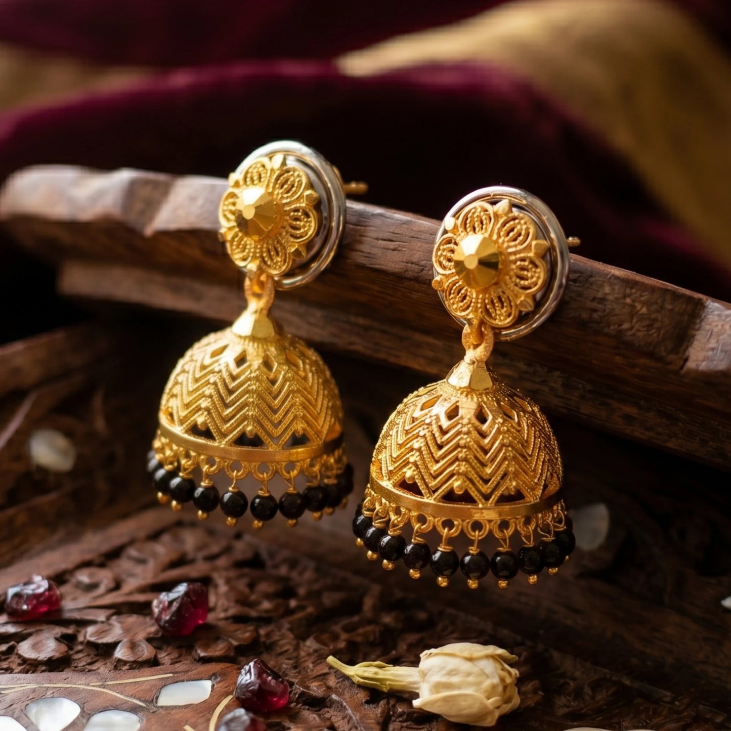 Gold plated traditional Jimikki/jhumka  earrings with black beads and intricate designs on a wooden surface