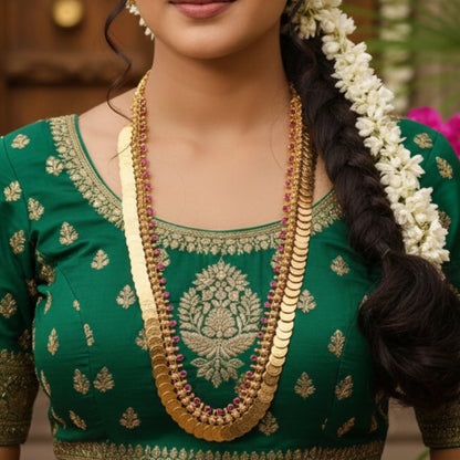 Woman wearing a green embroidered blouse with gold plated Traditional Kasu Mala jewelry and a floral hair accessory.