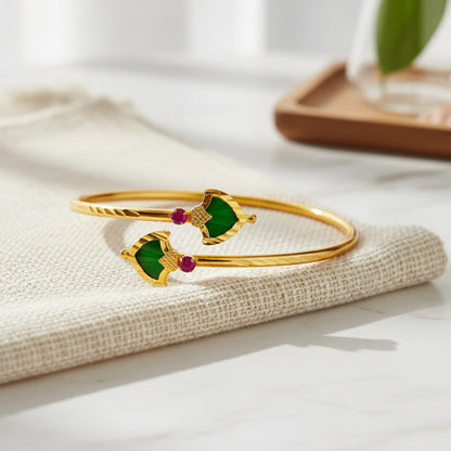 Gold bracelet/Cuff/Torque with green palakka and red stones on a textured surface