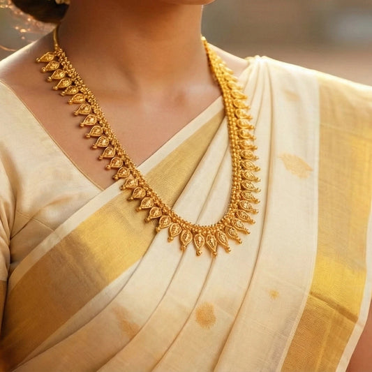 Gold plated necklace on a person wearing a cream and gold saree with a blurred background