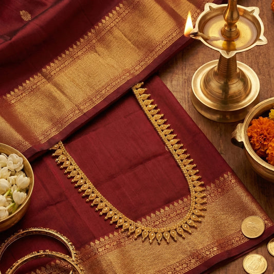 Gold Plated necklace Displayed on a Maroon saree with gold border on a wooden surface with a lit lamp and coins.