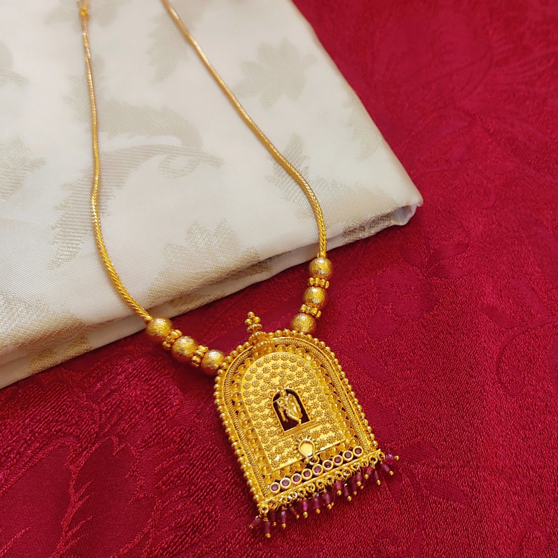 Gold plated traditional krishna temple arch necklace with a pendant on a red fabric background