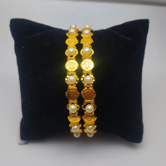 Pair of gold plated bangles with lakshmi motif and pearl in a intricate design on a black cushion