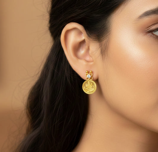 Close-up of a woman wearing gold plated Lakshmi Coin earrings with a blurred background
