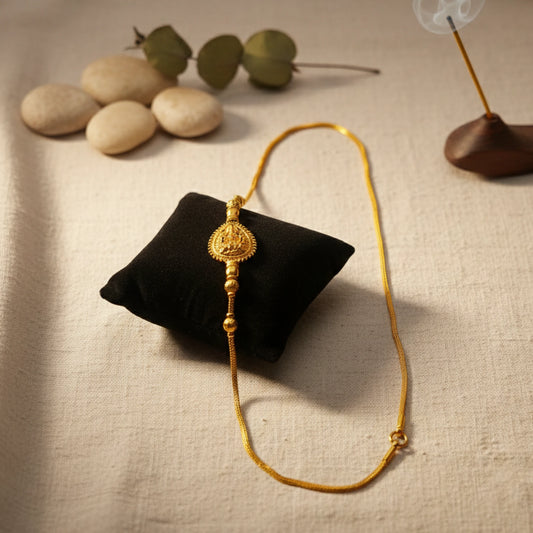 Gold plated necklace with Lakshmi motif on a black pillow with stones and eucalyptus leaves in the background