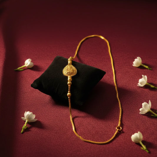 Gold plated neckchain with lakshmi motif on a black pillow with white flowers on a red background
