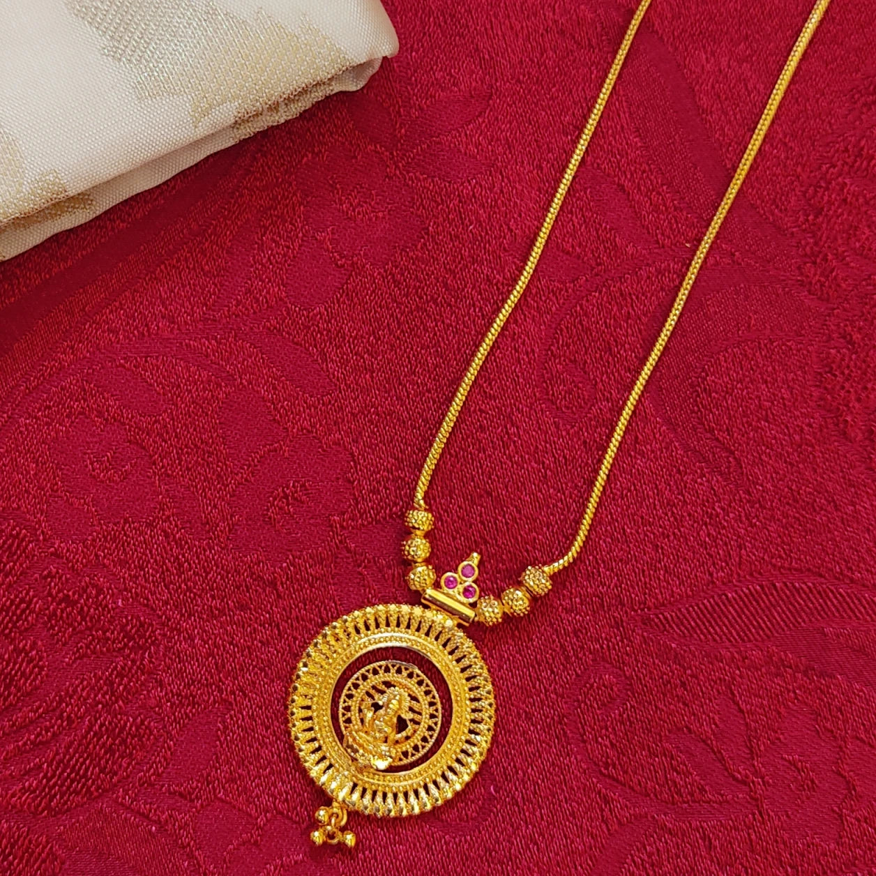 Gold plated necklace with a circular pendant with Lakshmi Motif on a red fabric background