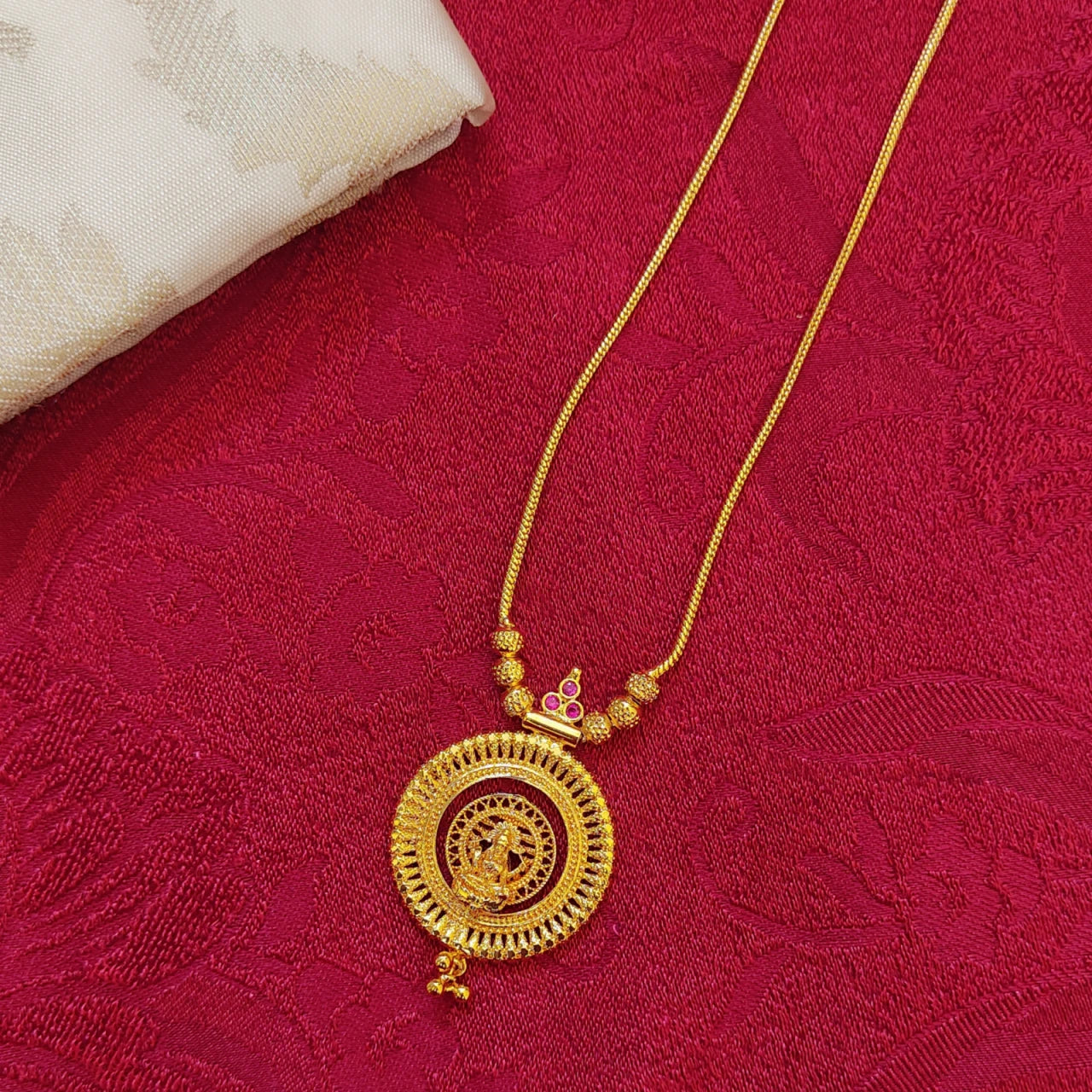 Gold plated necklace with a circular pendant with Lakshmi Motif on a red fabric background