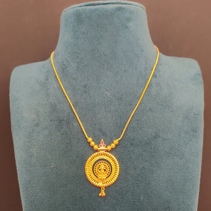 Gold plated necklace with a pendant with Lakshmi motif on a green velvet mannequin against a brown background