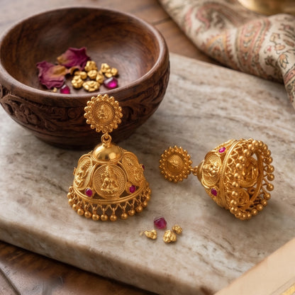 Gold plated Traditional Lakshmi Temple Jimikki/Jhumka earrings with red stones on a marble surface next to a wooden bowl