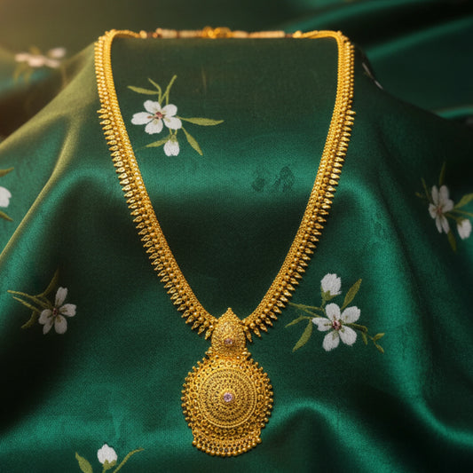 Gold plated long haram necklace with a mandala pendant  on a green fabric background with floral pattern