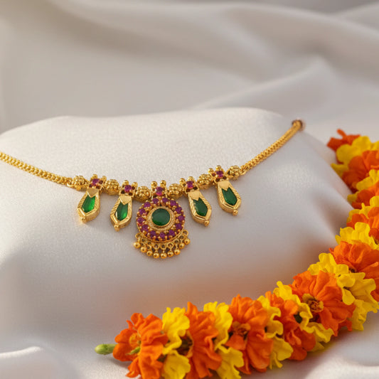 Gold plated Choker necklace with green  Naga Padam and ruby red stones on a white cushion with orange and yellow flowers.