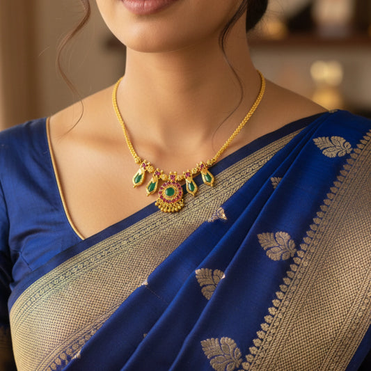 Woman wearing a blue saree with gold plated choker necklace with green naga padam and ruby red stones jewelry, focusing on the necklace.