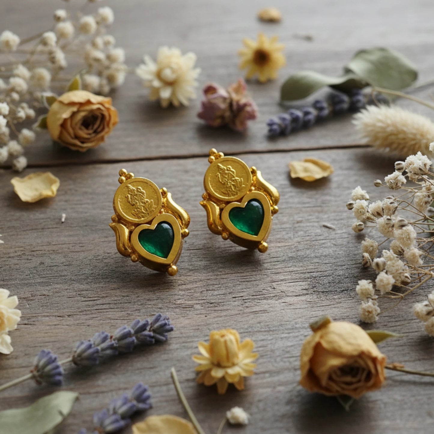 Gold plated earrings with green palakka heart stones on a wooden surface with flowers