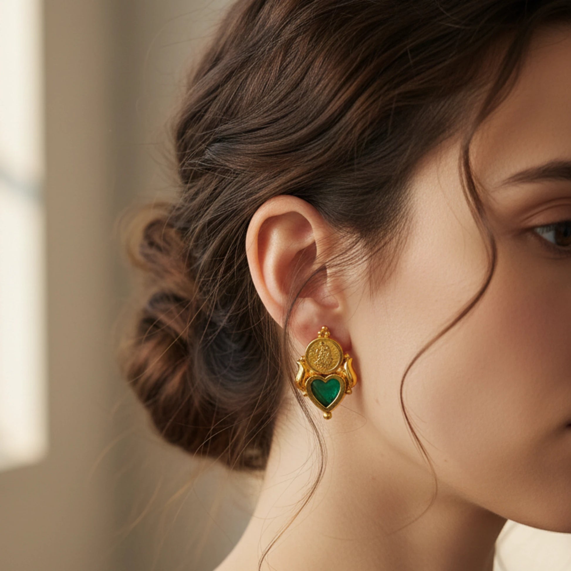 Close-up of a woman wearing a gold plated palakka heart earring with a green inlay
