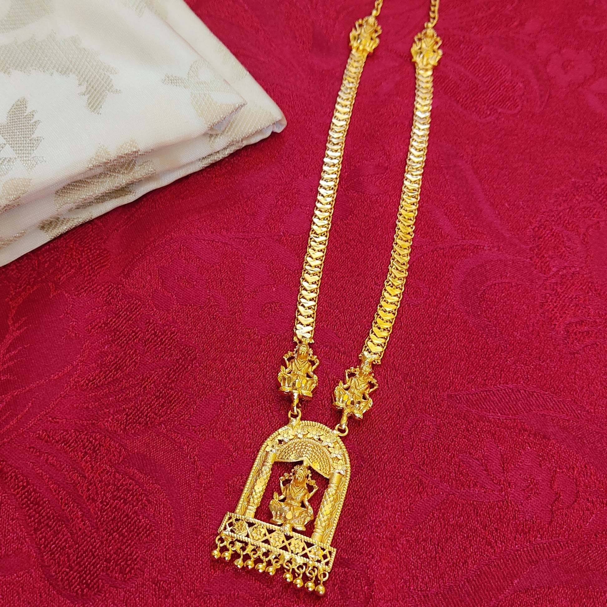 Gold plated necklace with a Lakshmi pendant on a red fabric background