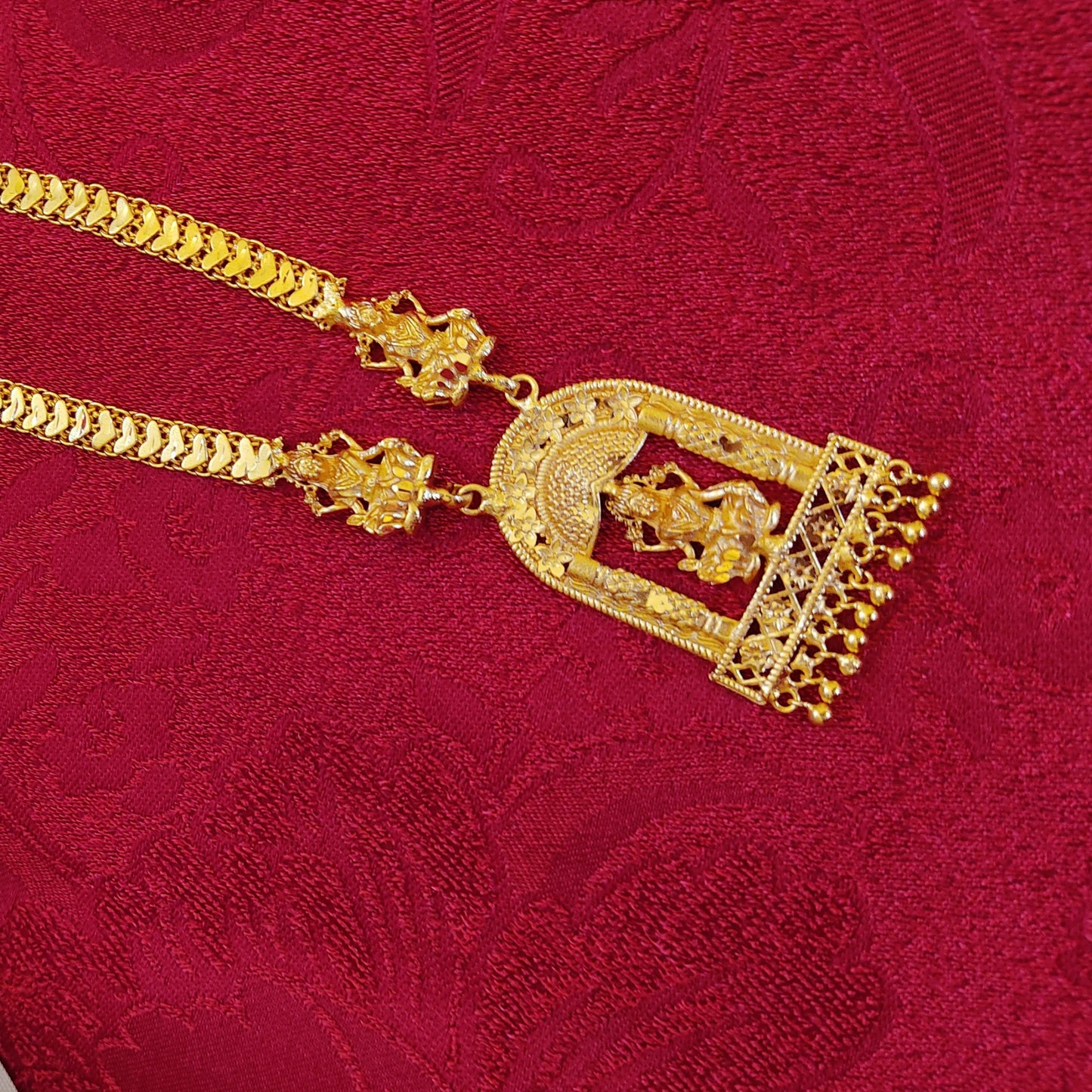 Gold plated necklace with intricate design and Lakshmi Pendant on a red textured background