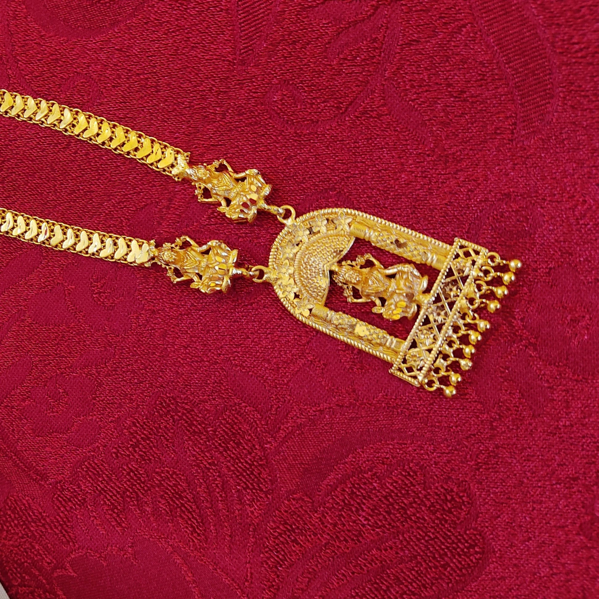 Gold plated necklace with intricate design and Lakshmi Pendant on a red textured background