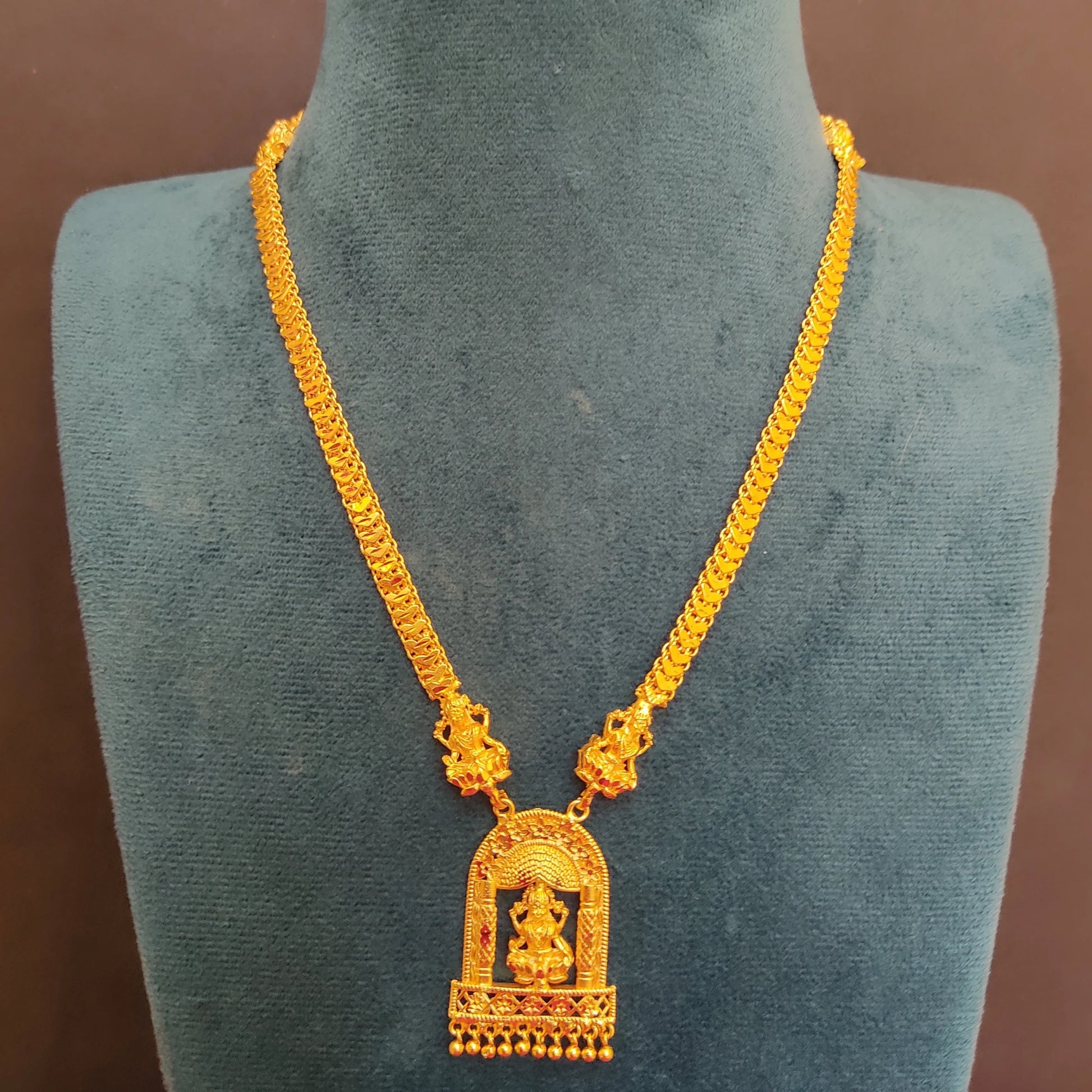 Gold plated necklace with a temple arch lakshmi pendant on a green mannequin against a brown background
