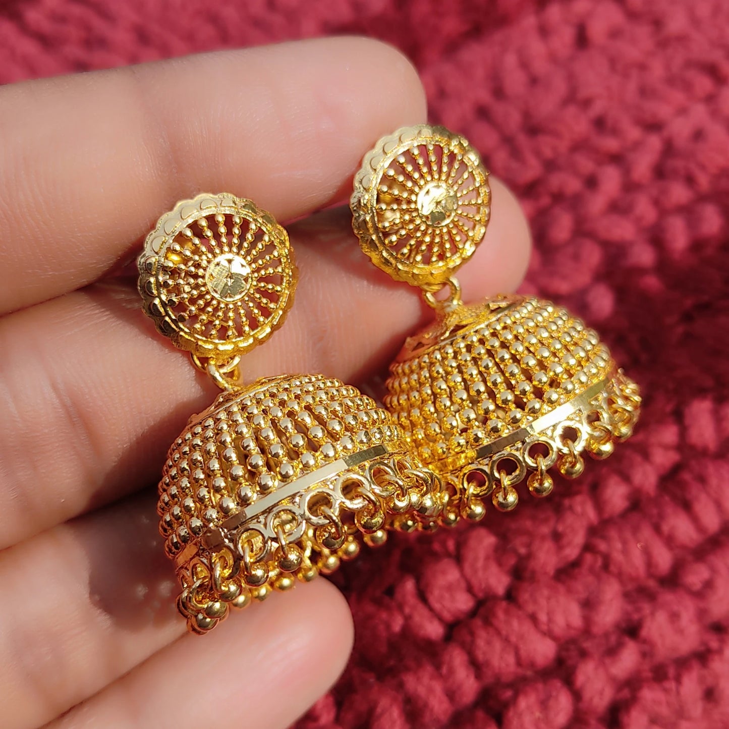 Gold plated Traditional Classic Bell Jimikki/Jhumka earrings held in a hand against a red textured background