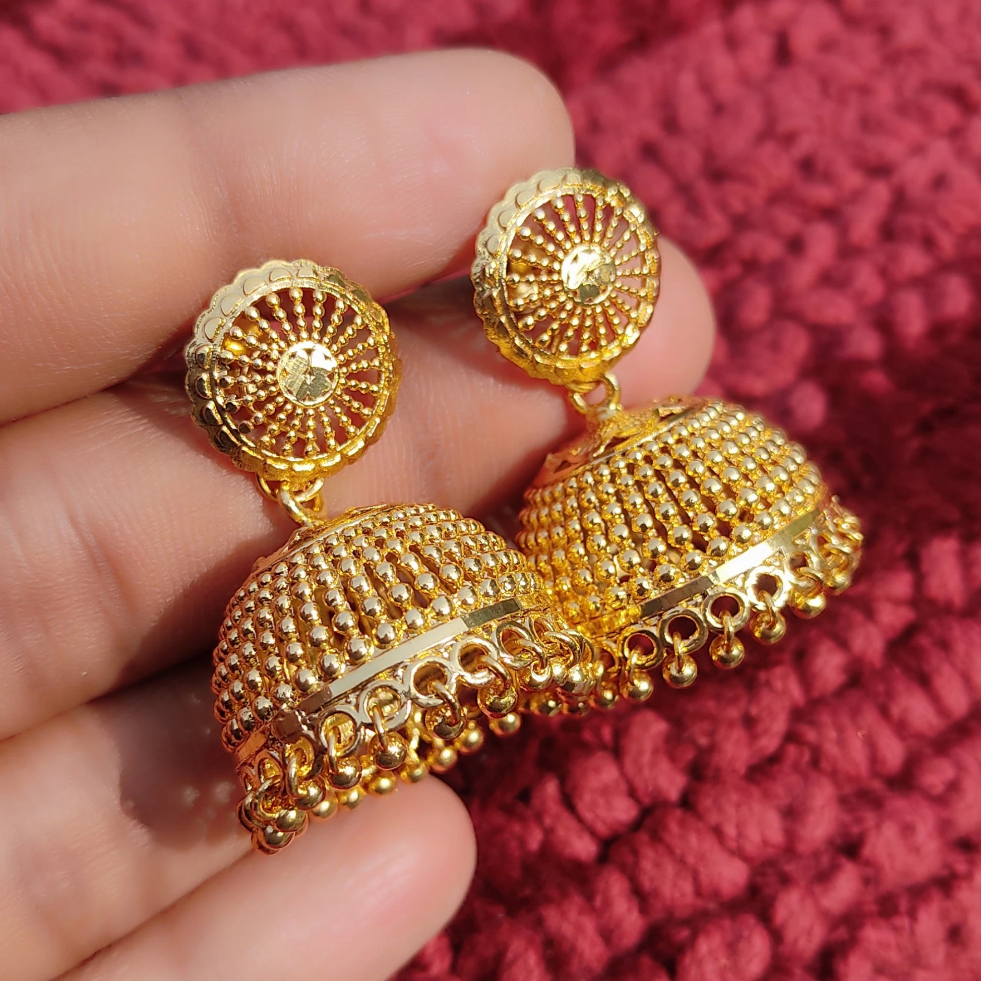 Gold plated Traditional Classic Bell Jimikki/Jhumka earrings held in a hand against a red textured background