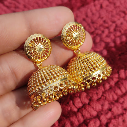 Gold plated Traditional Classic Bell Jimikki/Jhumka earrings held in a hand against a red textured background