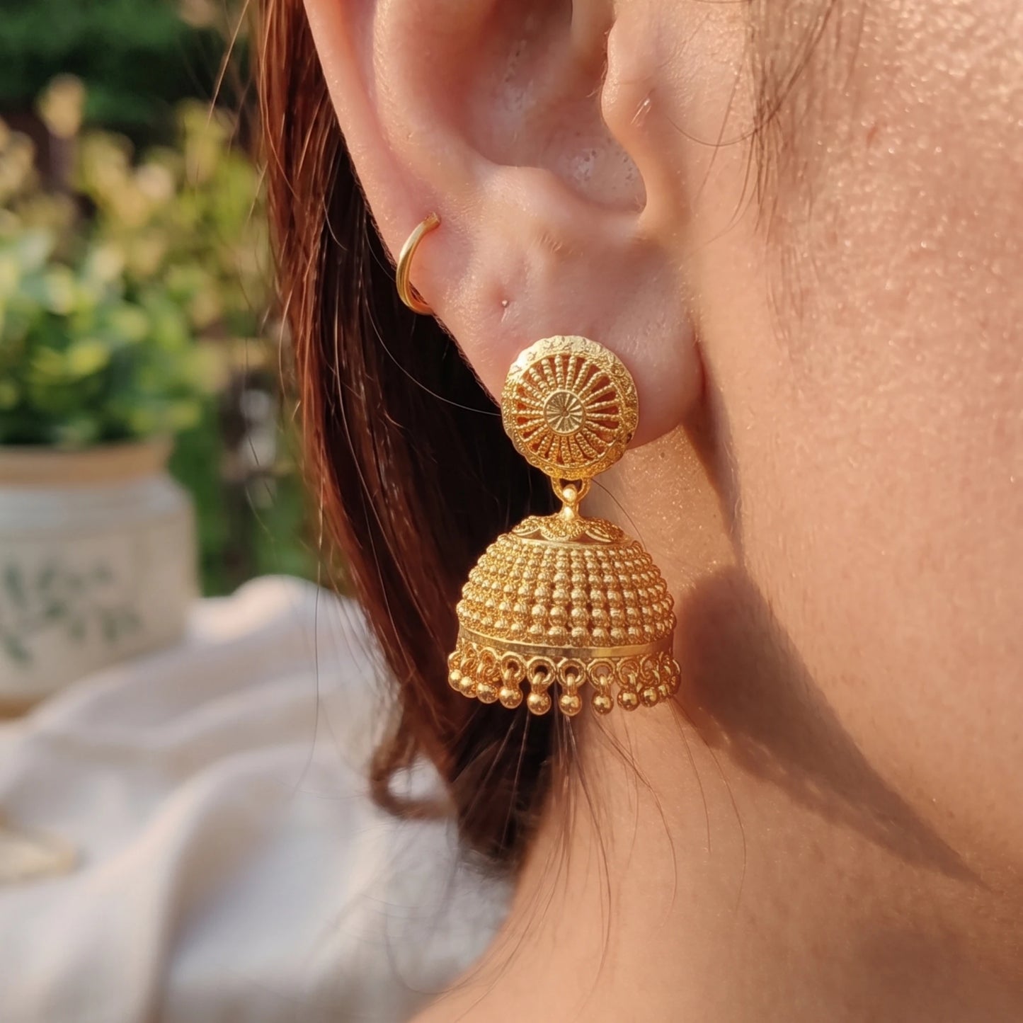 Gold plated Traditional Classic Bell Jimikki/Jhumka earrings worn by a person with a blurred natural background