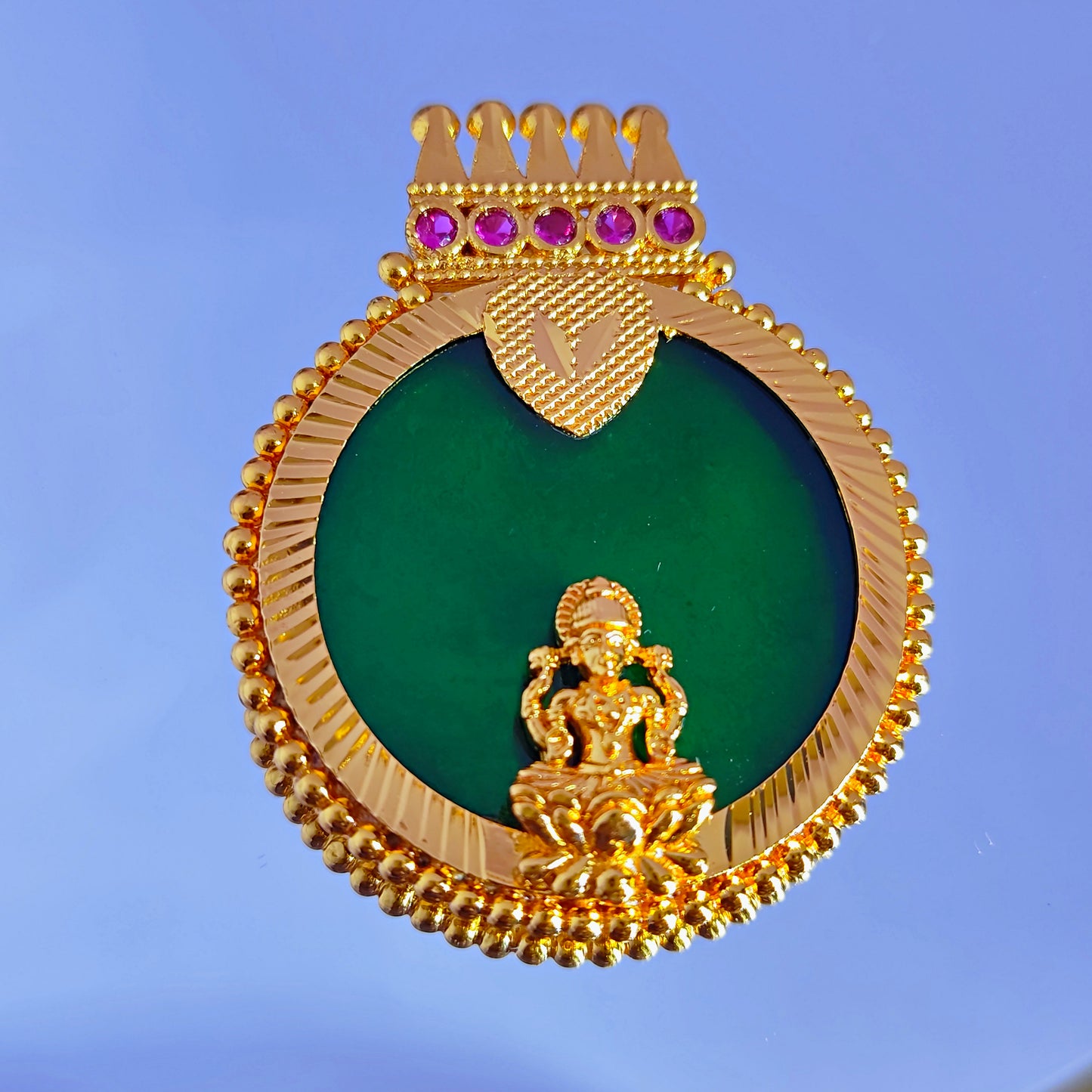 Gold plated pendant with green stone and pink gemstones on a blue background