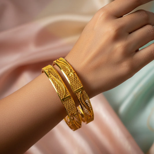 Gold plated bangles with intricate texturing on a wrist with a soft pink background