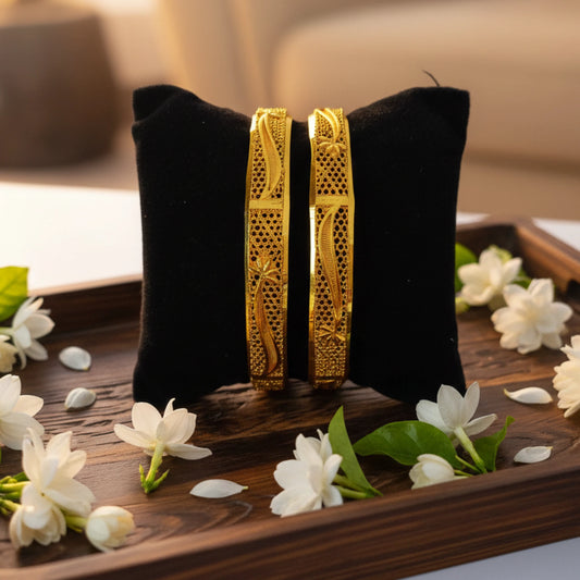 Gold plated bangles with traditional intricate texturing done on a black pillow with white flowers around