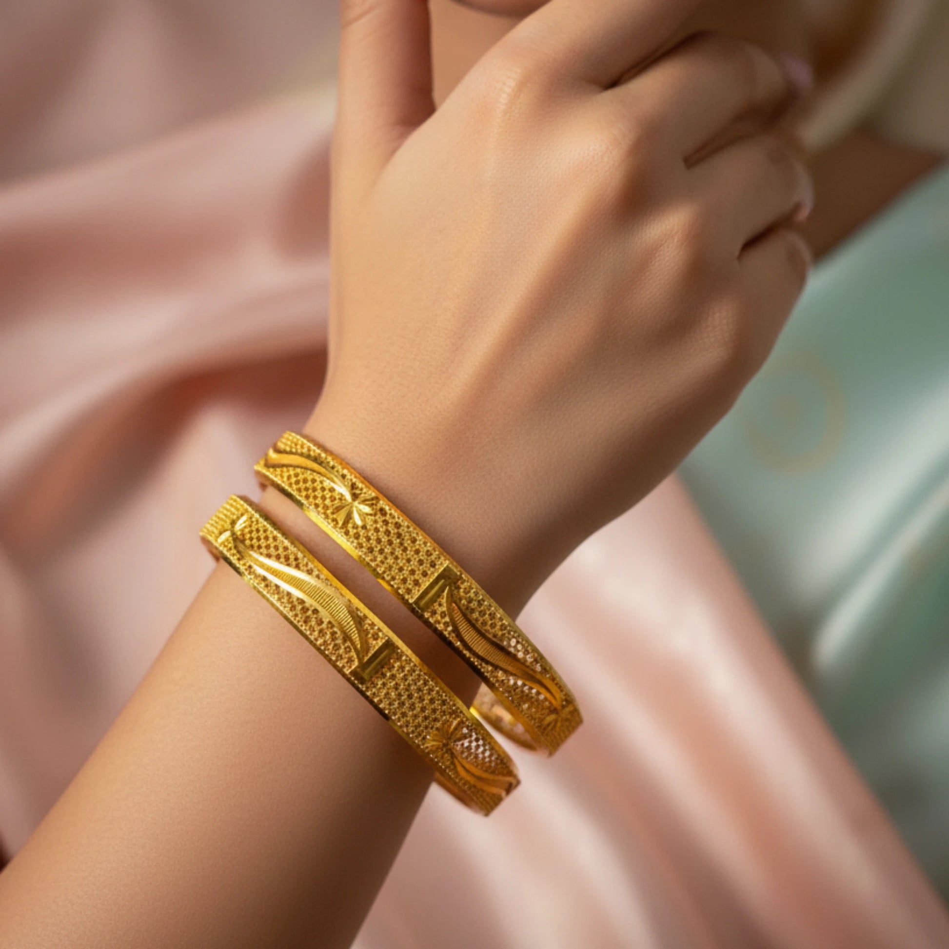 Gold plated bangles with intricate texturing on a wrist with a soft background