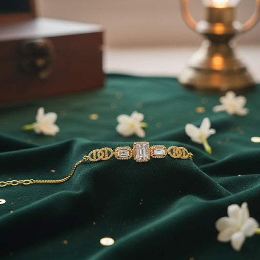 Gold plated bracelet on a green fabric surface with white flowers and a vintage suitcase in the background.