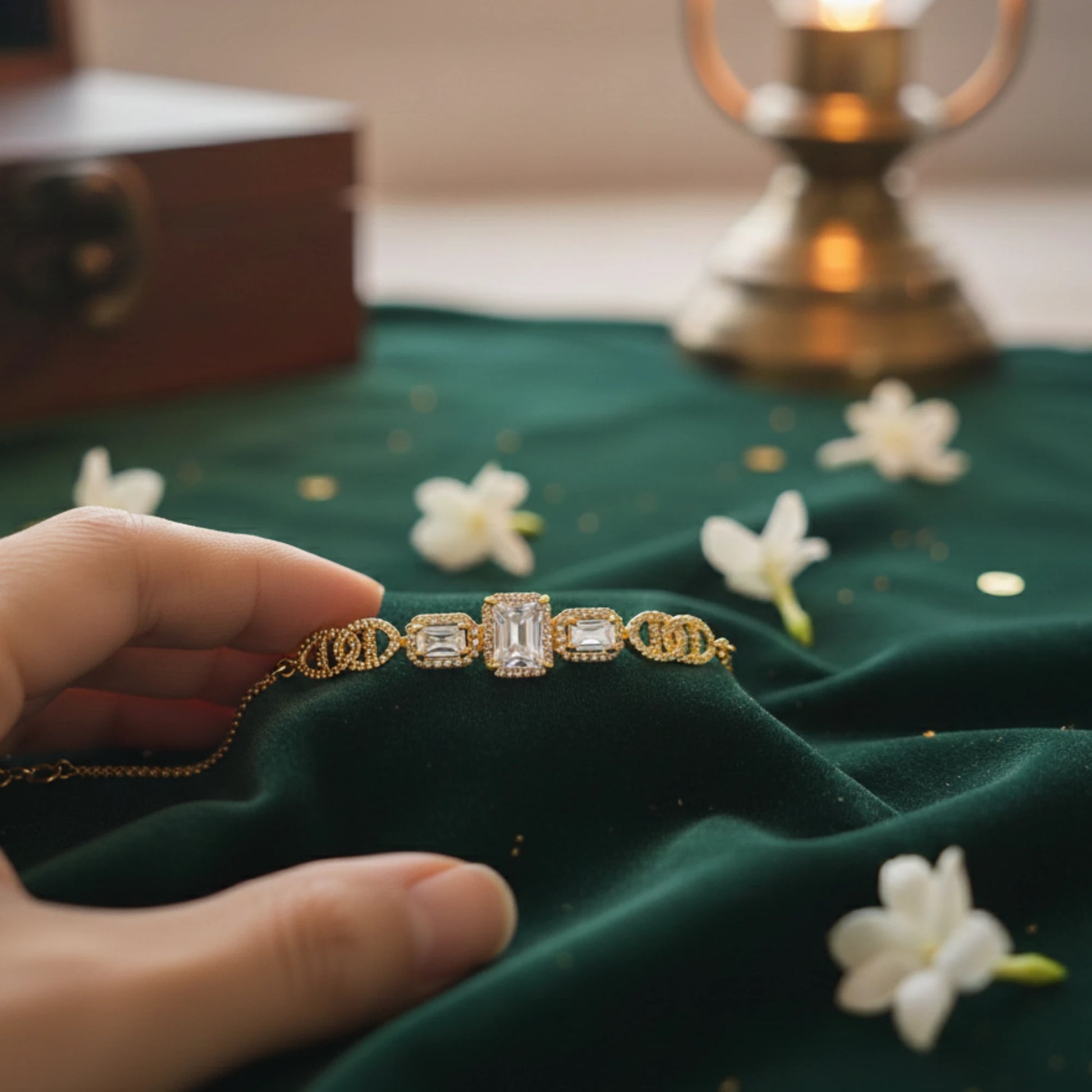 Gold plated bracelet with gemstones held by a hand on a green fabric background with flowers.