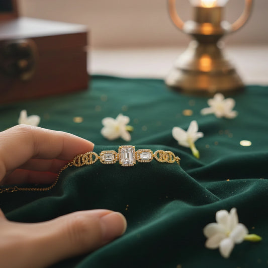 Gold plated bracelet with gemstones held by a hand on a green fabric background with flowers.