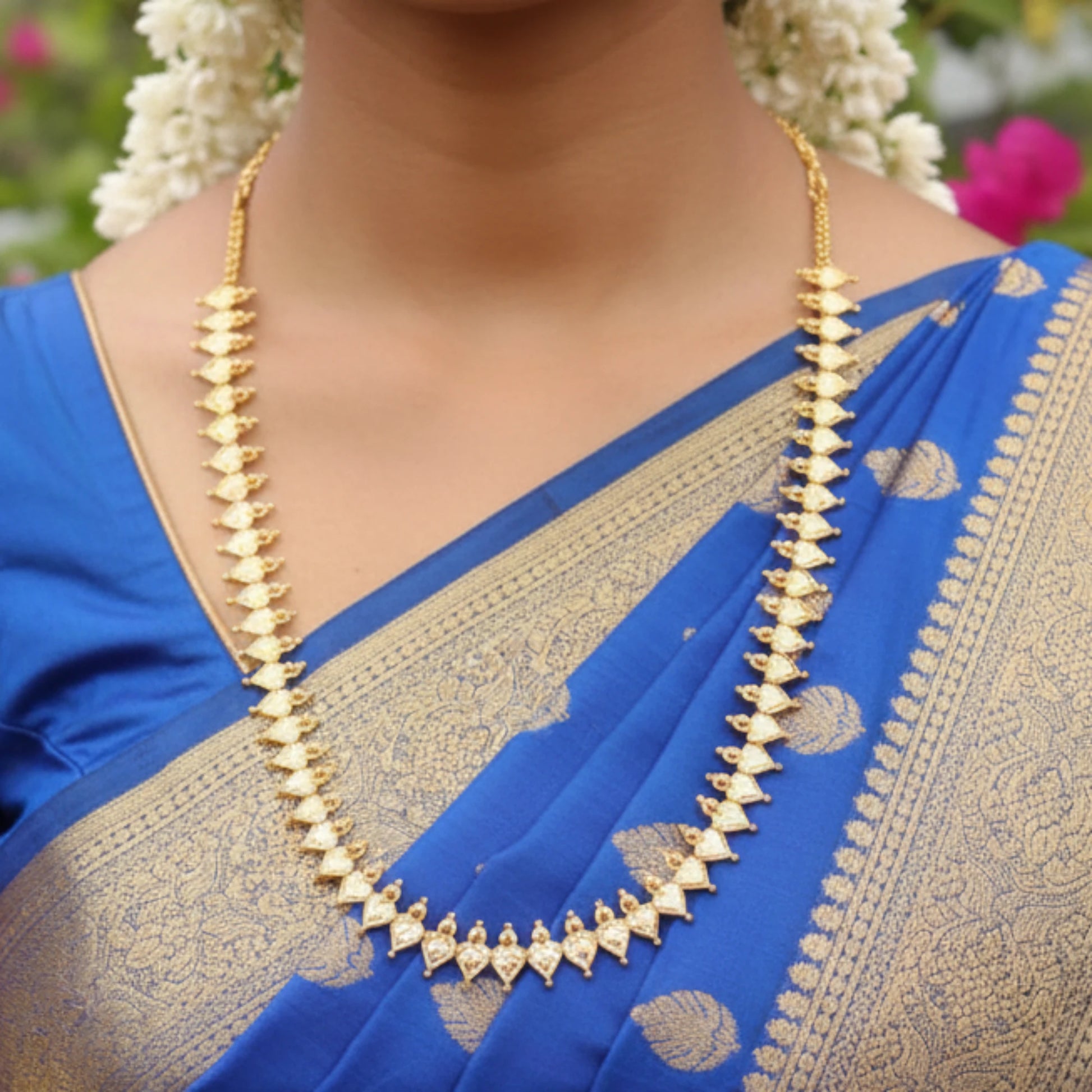 Woman wearing a blue saree with gold border and a gold plated necklace.
