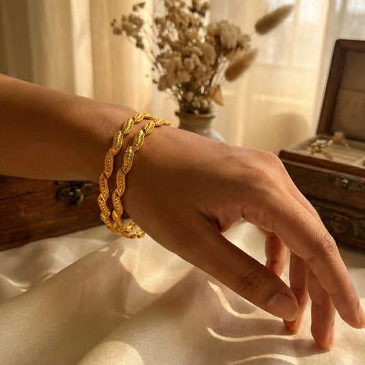 Hand wearing a gold plated bangle set with a soft, blurred background