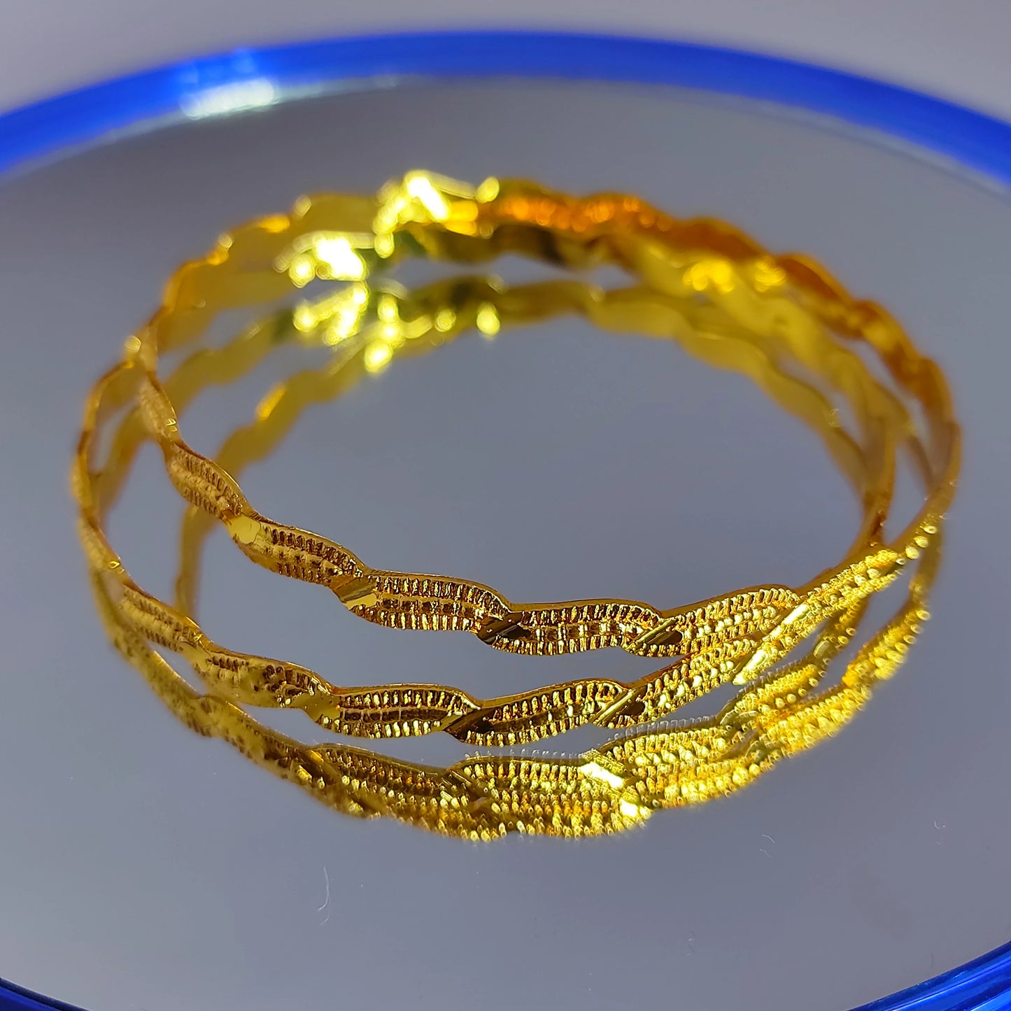 Gold plated bangles on a reflective surface