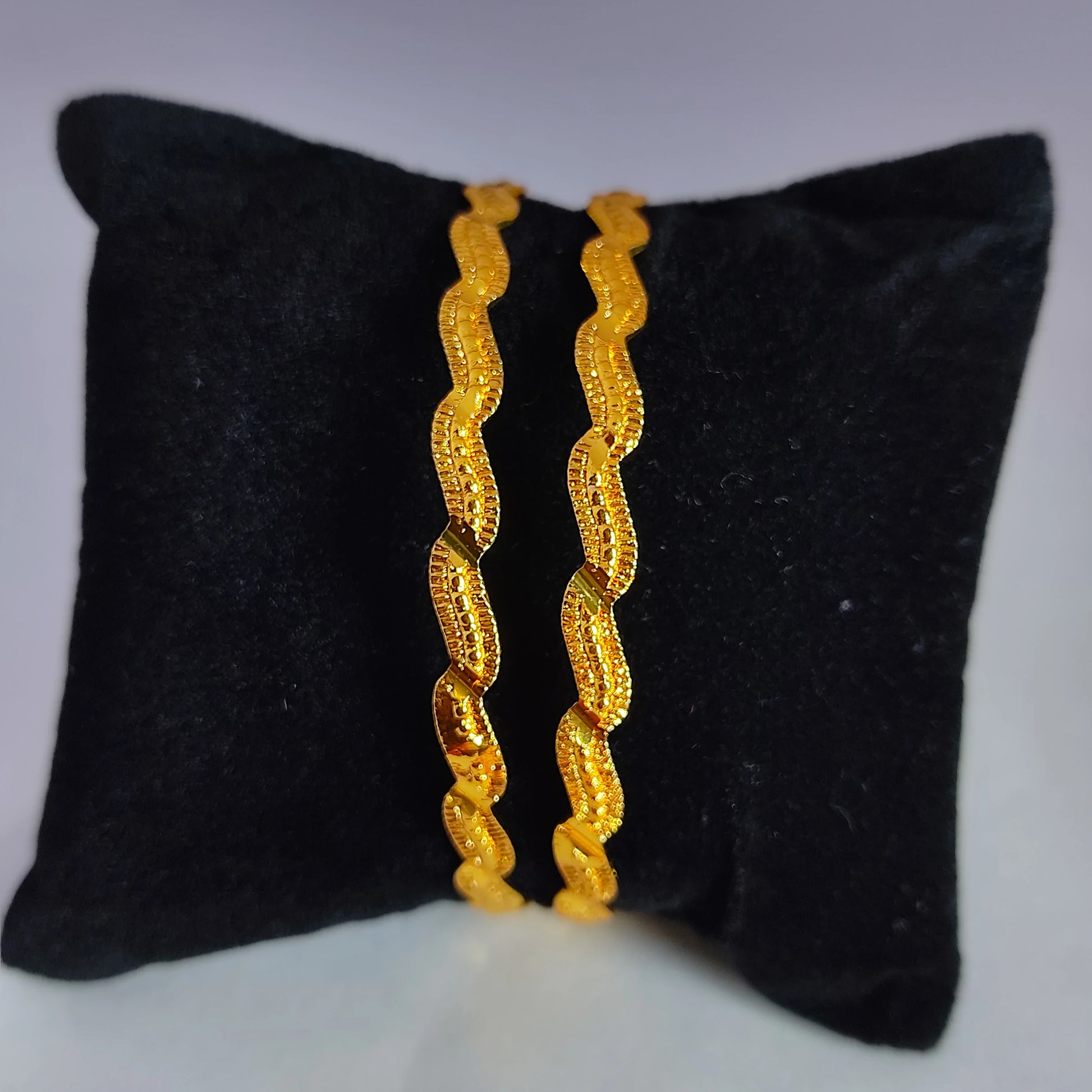 Pair of gold plated bangles on a black cushion
