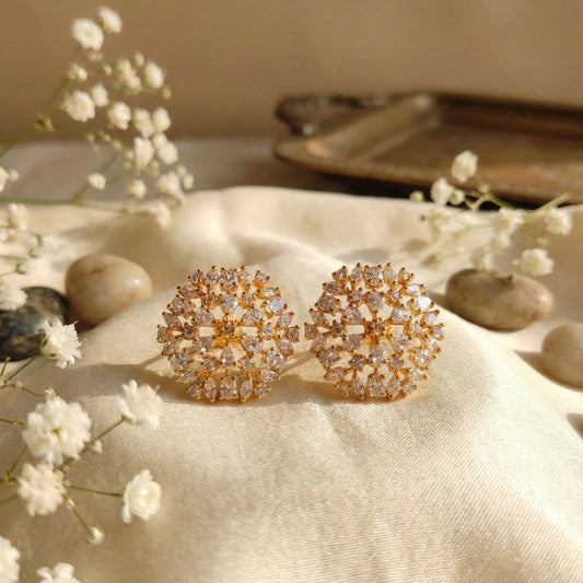 Gold plated earrings with gemstones on a beige fabric background with small white flowers and stones.