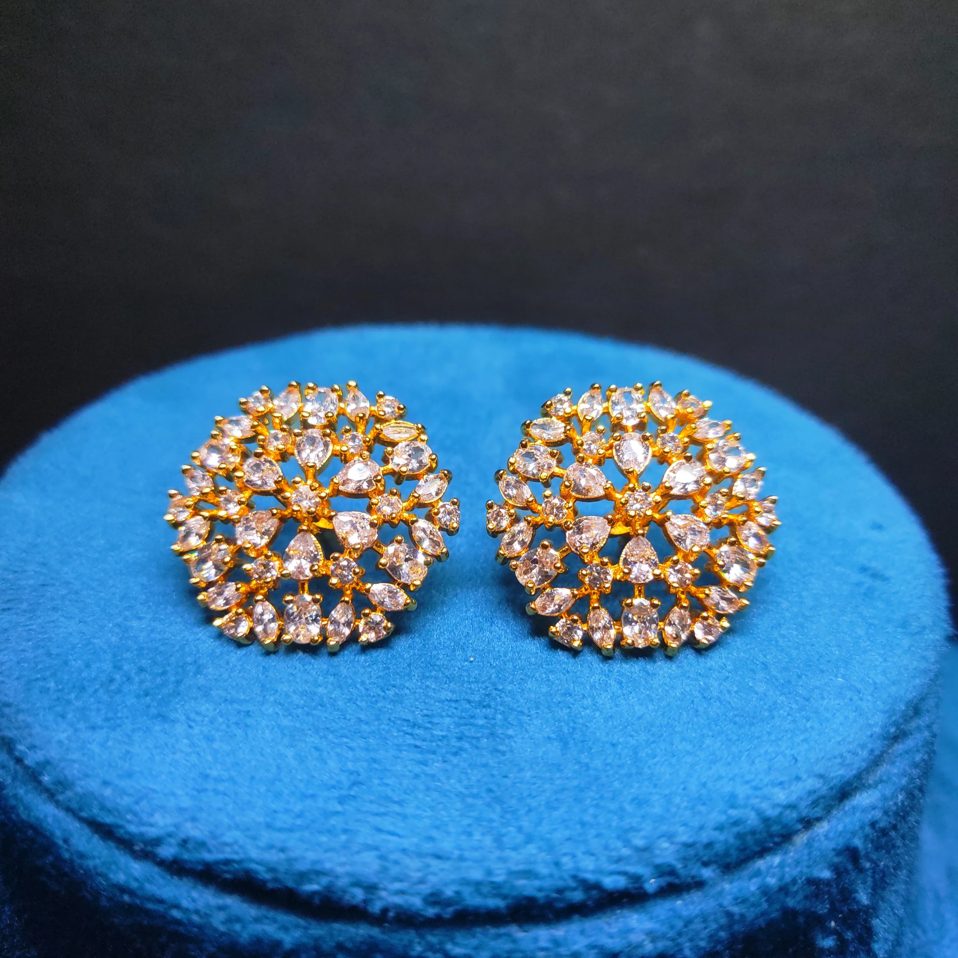 Gold Plated AD earrings on a blue cushion with a black background