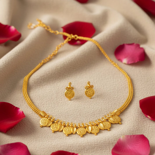 Gold toned choker necklace and earrings on a beige fabric background with red rose petals