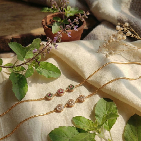 Gold toned Mugappu chains with gemstones on a beige fabric background with plants