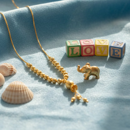 Gold plated beaded necklace with pendant on a blue fabric background with 'LOVE' blocks and seashells.